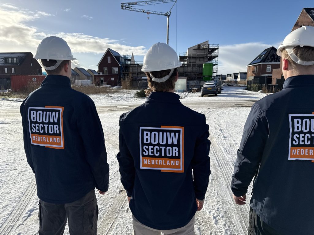 Drie vakmensen van Bouwsector Nederland met witte helm op een besneeuwde bouwstraat met een bouwkraan